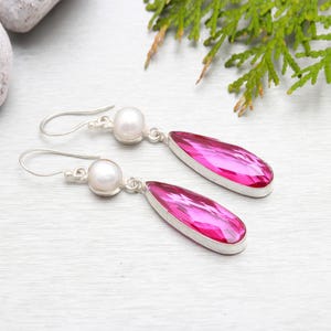 May include: A pair of silver dangle earrings with pink teardrop-shaped gemstones and white pearl accents.