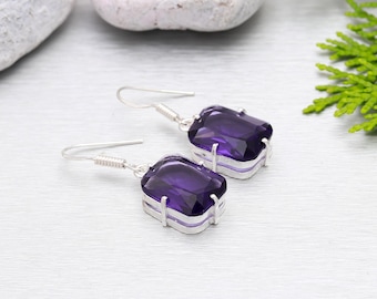 May include: A pair of silver dangle earrings with purple gemstone drops. The earrings have a simple design and are perfect for everyday wear.