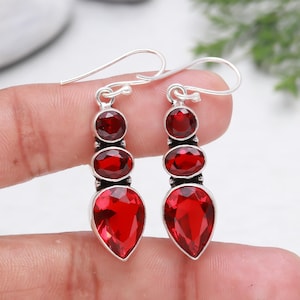 Puede incluir: Un par de pendientes de plata con gotas de piedras preciosas rojas. Los pendientes tienen tres piedras preciosas redondas y una piedra preciosa en forma de pera.