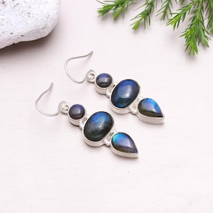 May include: A pair of silver dangle earrings with three iridescent blue labradorite stones. The stones are oval, round, and teardrop shaped.