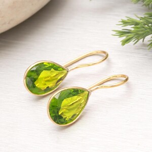 Puede incluir: Un par de pendientes dorados con piedras preciosas verdes claras en forma de pera. Las piedras preciosas est&aacute;n engastadas en un metal dorado y tienen forma de l&aacute;grima. Los pendientes tienen un dise&ntilde;o sencillo y elegante.