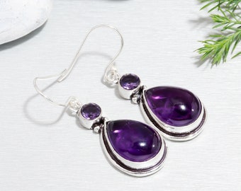 May include: A pair of silver dangle earrings featuring teardrop-shaped amethyst gemstones. The larger stones are set in a silver bezel, and the earrings have a simple hook fastening.