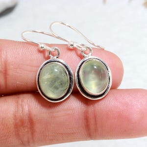 May include: A pair of silver earrings with green gemstone oval drops. The earrings have a simple design and are perfect for everyday wear.
