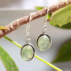 May include: A pair of silver dangle earrings with oval-shaped green gemstones. The earrings have a simple design and are perfect for everyday wear.
