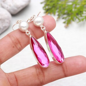 May include: A pair of silver dangle earrings with pink teardrop-shaped gemstones and white pearl accents.