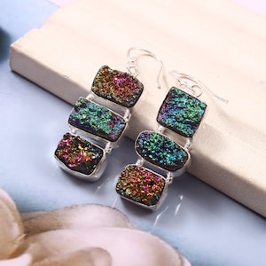 May include: A pair of silver dangle earrings with iridescent, multi-colored, rectangular stones. The stones are layered on top of each other, creating a cascading effect.