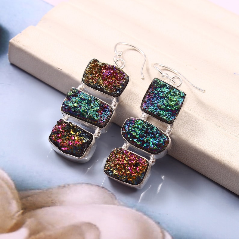 May include: A pair of silver dangle earrings with iridescent, multi-colored, rectangular stones. The stones are layered on top of each other, creating a cascading effect.