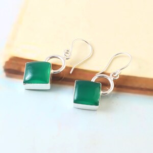 May include: A pair of silver dangle earrings with square green gemstone accents.