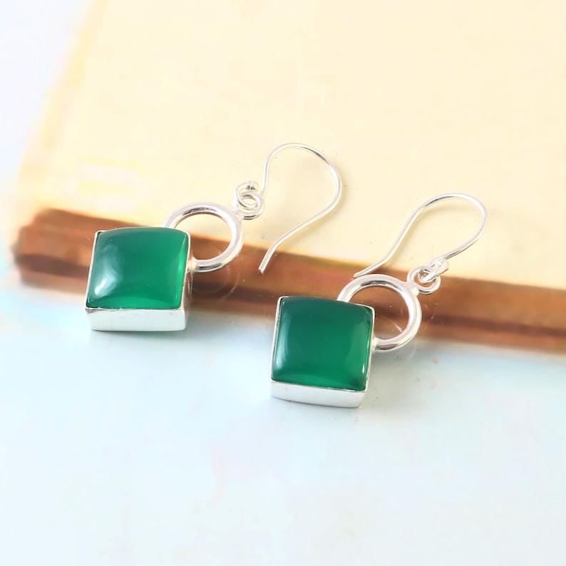 May include: A pair of silver dangle earrings with square green gemstone accents.