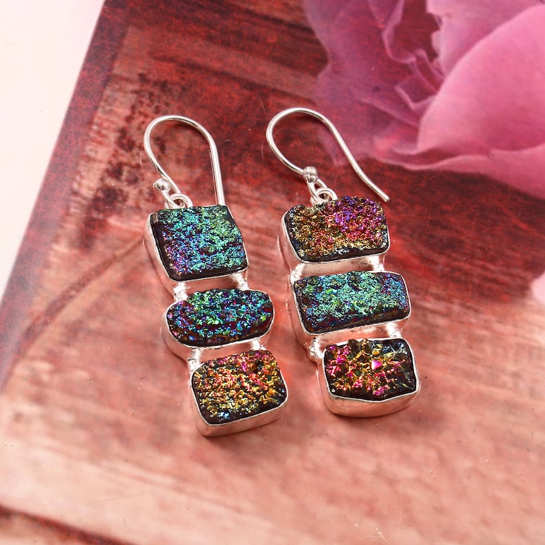 May include: A pair of silver dangle earrings with three iridescent, faceted, rectangular stones. The stones are a mix of green, blue, purple, and red.