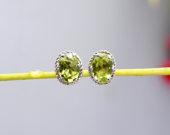 Könnte beinhalten: Ein Paar silberne Ohrringe mit grünen ovalen Peridot-Edelsteinen, die in einem zarten Seil-Design gefasst sind.