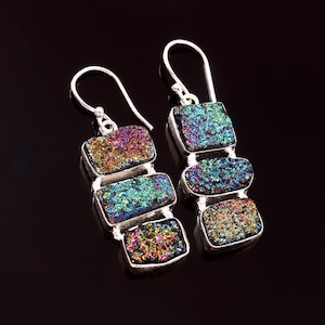 May include: A pair of silver earrings with iridescent gemstone drops. Each earring features three rectangular shaped stones in shades of blue, green, purple, and gold.