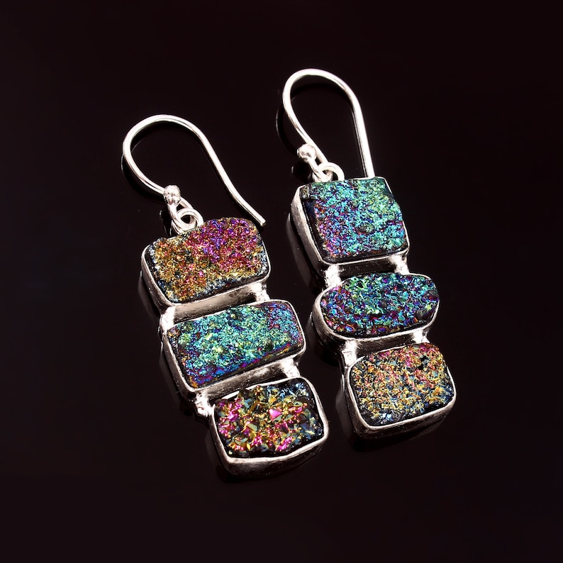 May include: A pair of silver earrings with iridescent gemstone drops. Each earring features three rectangular shaped stones in shades of blue, green, purple, and gold.