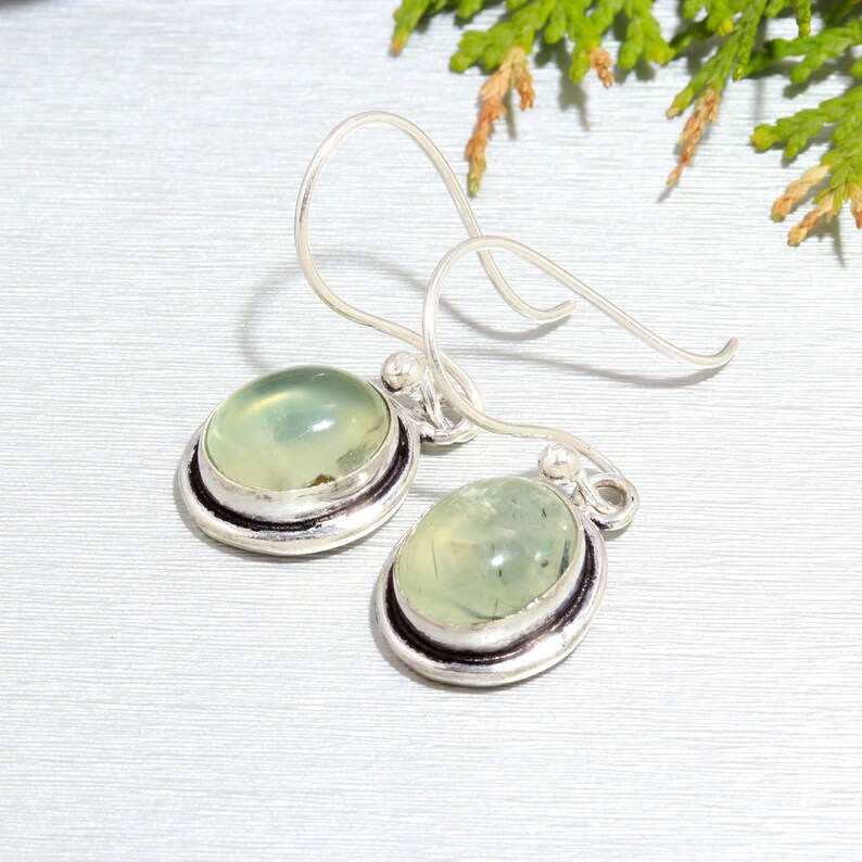 May include: A pair of silver earrings with green aventurine stones. The stones are oval shaped and set in a silver bezel. The earrings have a simple hook closure.
