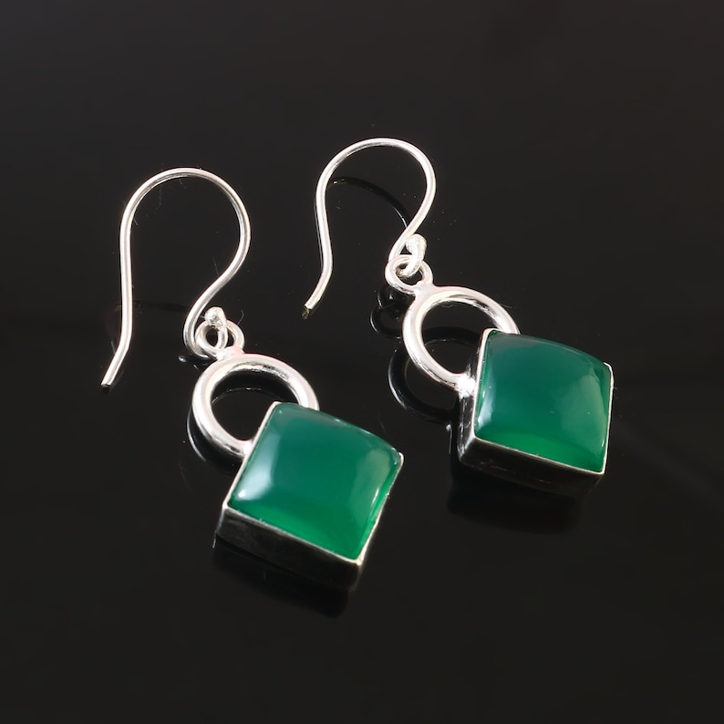 May include: A pair of silver dangle earrings with green gemstone square drops. The earrings have a simple hoop design.