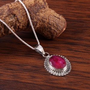 Puede incluir: Un collar de cadena de plata con un colgante que presenta una gran piedra preciosa roja ovalada engastada en un marco de filigrana de plata.