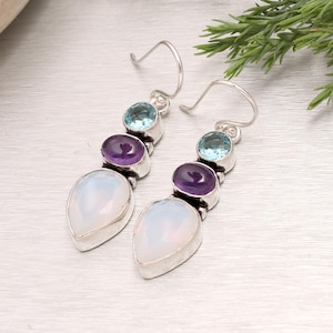 May include: A pair of silver earrings with a drop design. Each earring features a light blue, purple, and white gemstone. The gemstones are set in silver and are connected by silver links. The earrings have a hook closure.
