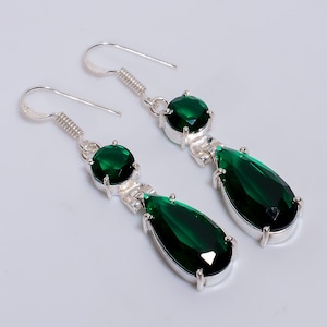 May include: A pair of drop earrings with vivid green gemstones. Each earring features a round stone, a silver connecting element, and a large teardrop-shaped stone. The earrings have a silver hook closure.