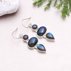 May include: A pair of silver dangle earrings with three iridescent blue labradorite stones. The stones are oval, round, and teardrop shaped.