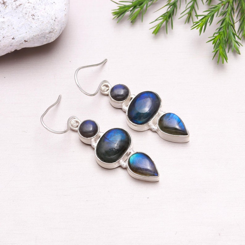 May include: A pair of silver dangle earrings with three iridescent blue labradorite stones. The stones are oval, round, and teardrop shaped.