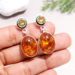 Op de afbeelding: Een paar zilveren oorbellen met amber en citrien edelstenen. De amberstenen zijn ovaalvormig en hebben een warme, honingkleur. De citrienstenen zijn rond en hebben een heldere, gele kleur.