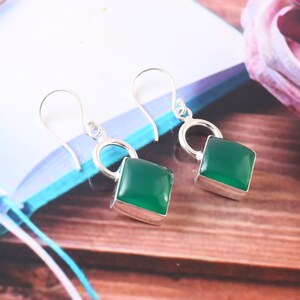 May include: A pair of silver dangle earrings with green gemstone square drops. The earrings have a simple hoop design.