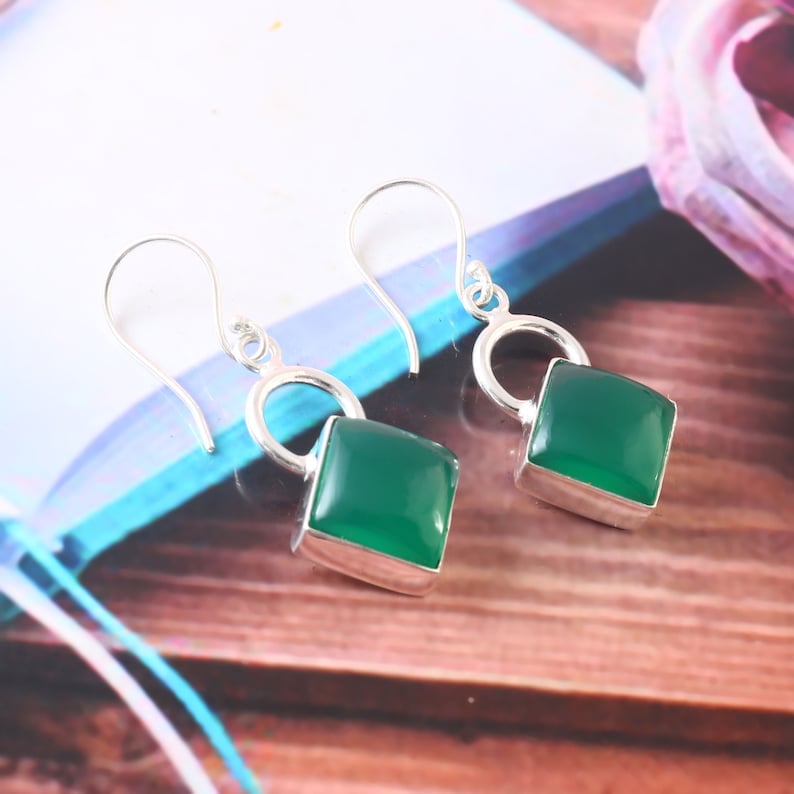 May include: A pair of silver dangle earrings with green gemstone square drops. The earrings have a simple hoop design.