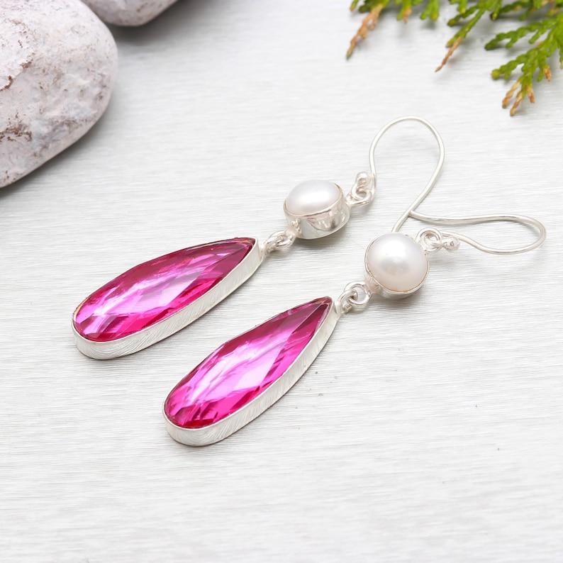 May include: A pair of silver dangle earrings with pink teardrop-shaped gemstones and white pearl accents.
