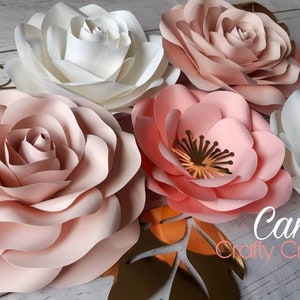 May include: Five large paper flowers in shades of pink and white. The flowers are arranged in a cluster on a wooden surface. The flowers are made of multiple layers of paper and have a delicate, ruffled appearance. The text "Cams Crafty Creations" is visible in the lower right corner of the image.