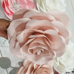 May include: A set of six paper flowers in shades of pink and white. The flowers are layered and have a delicate, romantic look. They are perfect for adding a touch of elegance to any event.