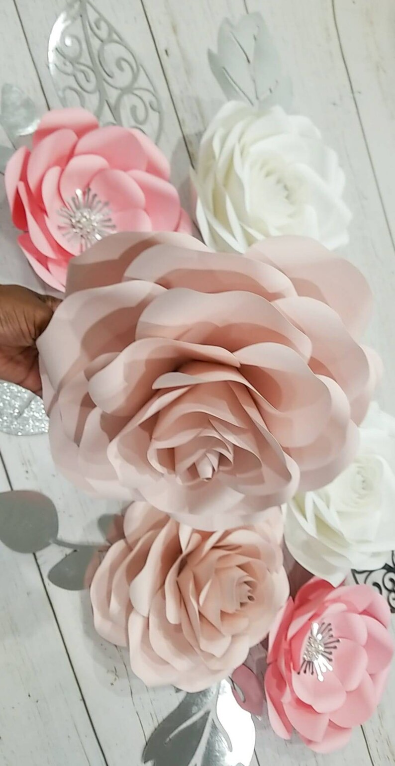 May include: A set of six paper flowers in shades of pink and white. The flowers are layered and have a delicate, romantic look. They are perfect for adding a touch of elegance to any event.