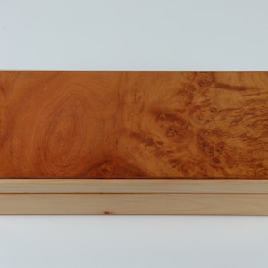May include: A wooden box with a light brown finish. The top of the box is made of a darker wood with a burl pattern.