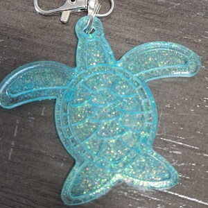 May include: A light blue glitter turtle keychain with a silver metal clasp.