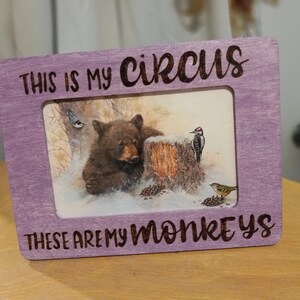 May include: A rectangular, light purple wooden picture frame with the text "THIS IS MY CIRCUS THESE ARE MY MONKEYS" in a handwritten font. The framed image depicts a bear, birds, and a tree stump.