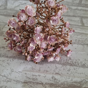 May include: A bunch of small, pale pink artificial flowers with brown stems. The flowers are clustered together and have a delicate, vintage look.