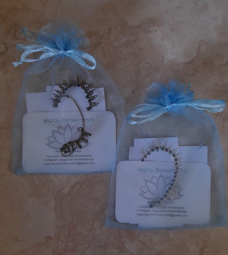 May include: Two small blue organza bags with silver ear cuffs inside. Each bag has a white card with the text "Magical Enchantments" and contact information for the seller.