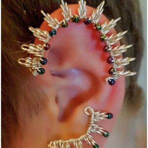 May include: A silver ear cuff with a spiky design and iridescent green and purple beads.