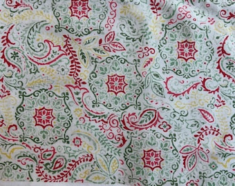 May include: A white fabric featuring a repeating pattern of red, sage green, and yellow floral and paisley motifs. The design includes intricate geometric shapes, stylised leaves, and swirling lines printed across the textured textile surface.