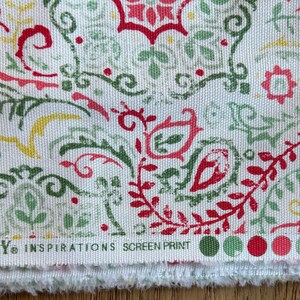 May include: A white fabric featuring a repeating screen-printed pattern of red, sage green, and yellow paisley and floral motifs. The bottom edge displays the text WAVERLY INSPIRATIONS SCREEN PRINT followed by a row of colored circular swatches.