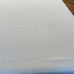 May include: A rectangular white tablecloth featuring a consistent, small-scale waffle weave texture across its entire surface. The fabric is draped flat, displaying a uniform grid pattern created by the raised woven structure of the textile material.