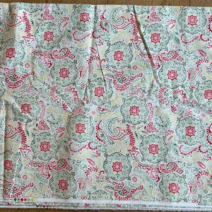 May include: A rectangular piece of fabric featuring a repeating pattern of red, green, and yellow paisley and floral motifs on a white background. The design includes intricate geometric shapes and swirling lines, with a finished edge at the bottom.
