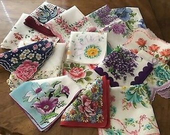 May include: A collection of folded square fabric handkerchiefs featuring various floral patterns in shades of pink, purple, blue, yellow, and green. The edges are finished with scalloped, embroidered, or plain hems in matching colors.