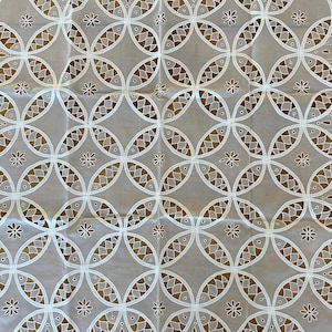 May include: A white, eyelet fabric with a repeating pattern of interlocking circles and small floral accents. The circles are filled with a brown, fish-scale design. The fabric is likely used for home decor or clothing.