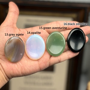 Peut inclure: Quatre pierres lisses, rondes et polies de diff&eacute;rentes couleurs, dont l'agate grise, l'opale, l'aventurine verte et l'obsidienne noire. Les pierres sont dispos&eacute;es en rang&eacute;e sur une main, avec les &eacute;tiquettes textuelles "13. agate grise", "14. opale", "15. aventurine verte" et "16. obsidienne noire" visibles au-dessus de chaque pierre.