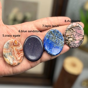 Peut inclure: Quatre types de pierres polies diff&eacute;rentes, dont l'agate folle, le gr&egrave;s bleu, le lapis-lazuli et la rhodonite, sont tenues dans une main. Les pierres sont toutes rondes et lisses, et elles pr&eacute;sentent une vari&eacute;t&eacute; de couleurs et de motifs.