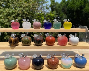 May include: A collection of 18 crystal apple figurines, each carved from a different type of gemstone. The apples are arranged on two wooden shelves, with each shelf displaying nine apples. The gemstones include tiger's eye, rose quartz, amethyst, clear quartz, and more.