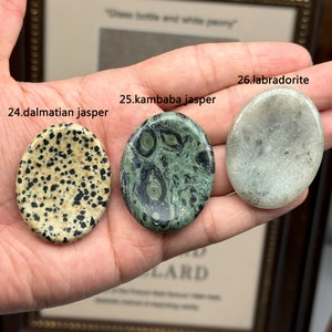 Peut inclure: Trois pierres polies, un jaspe dalmatien, un jaspe kambaaba et un labradorite, sont tenues dans une main. Les pierres sont rondes et lisses, avec une vari&eacute;t&eacute; de couleurs et de motifs.