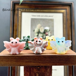 May include: Five small, hand-carved bat figurines made of different coloured stones. The bats are in a variety of colours, including pink, green, red, yellow, and blue.