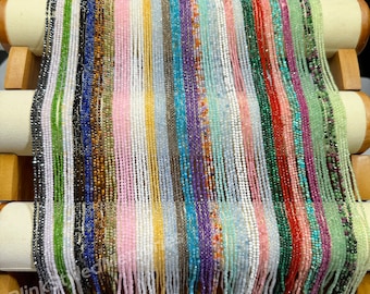 Puede incluir: Una variedad de hileras de cuentas de piedras preciosas expuestas en un soporte de madera. Las hileras están dispuestas en filas e incluyen colores como verde, azul, rosa, blanco y rojo.