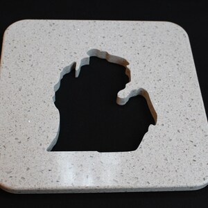 Op de afbeelding: Een vierkante, lichtgrijze onderzetter met een gespikkeld patroon. Het midden is uitgesneden in de vorm van de staat Michigan. De onderzetter heeft afgeronde hoeken en een glad oppervlak.